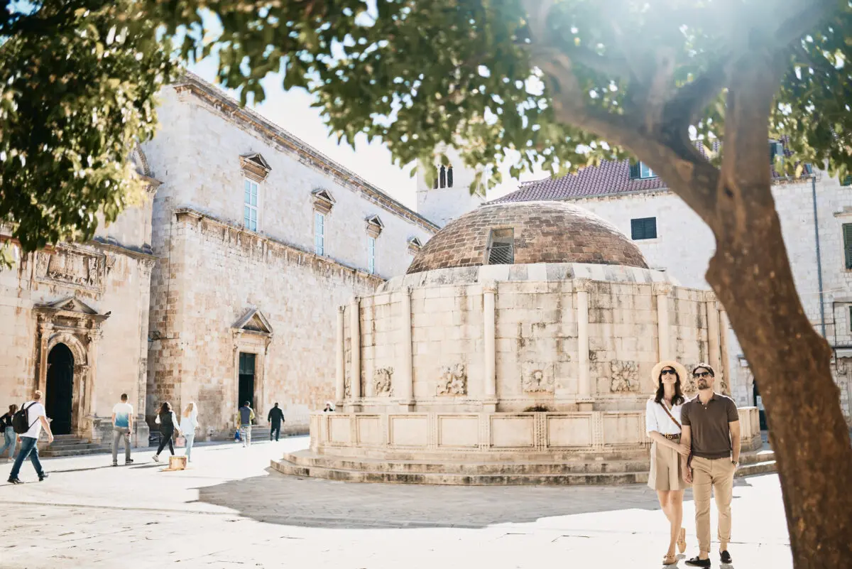 Couple in Dubrovnik, Croatia, near a historic fountain and building. Croatia Destination Wedding Hotel potential.