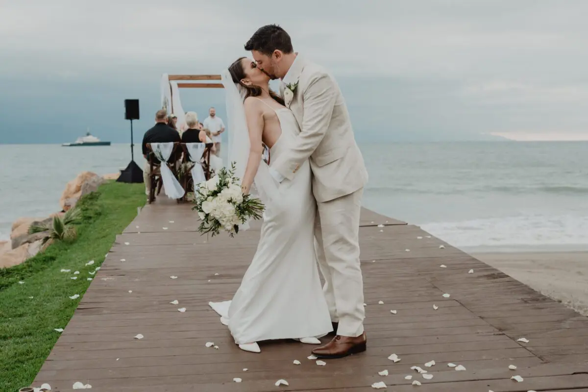 Newlyweds share a kiss during their Puerto Vallarta wedding ceremony at Velas Vallarta, with ocean views.