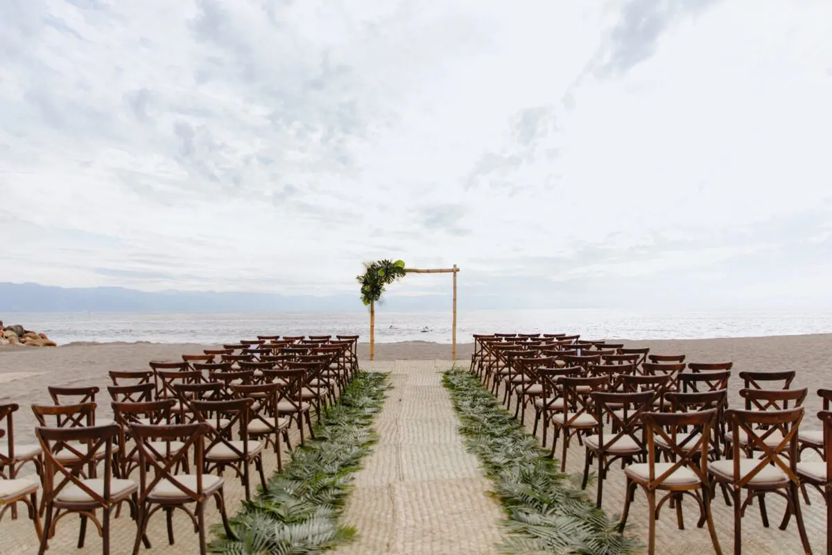Beach wedding ceremony setup at Velas Vallarta, Puerto Vallarta. Chairs face an arch decorated with greenery.