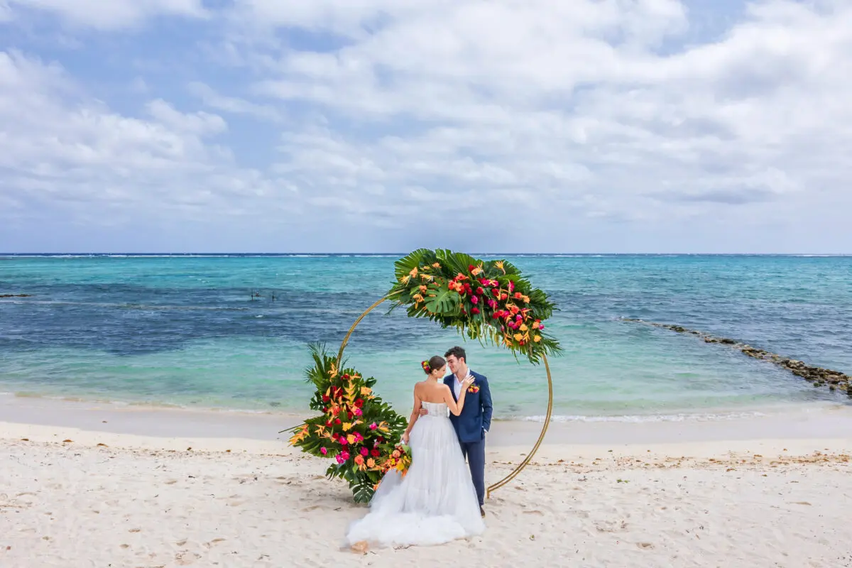 Bride and groom embracing at a Tulum wedding venue with a floral circle backdrop on the beach.