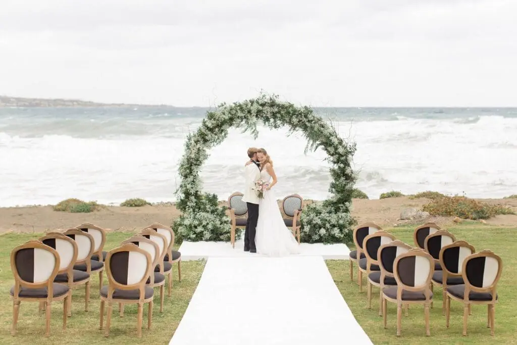 Bride and groom kissing under floral arch at European seaside wedding