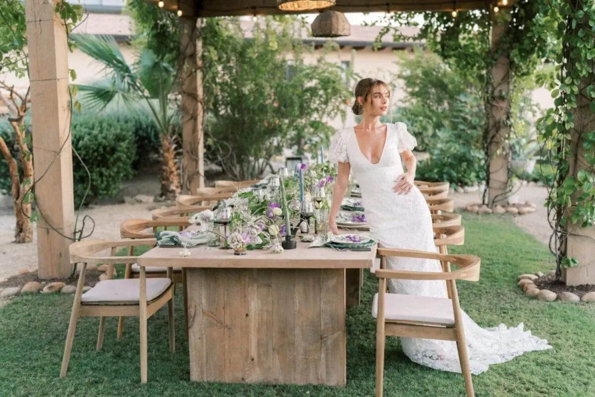 Bride in elegant garden with rustic wooden table set for celebration