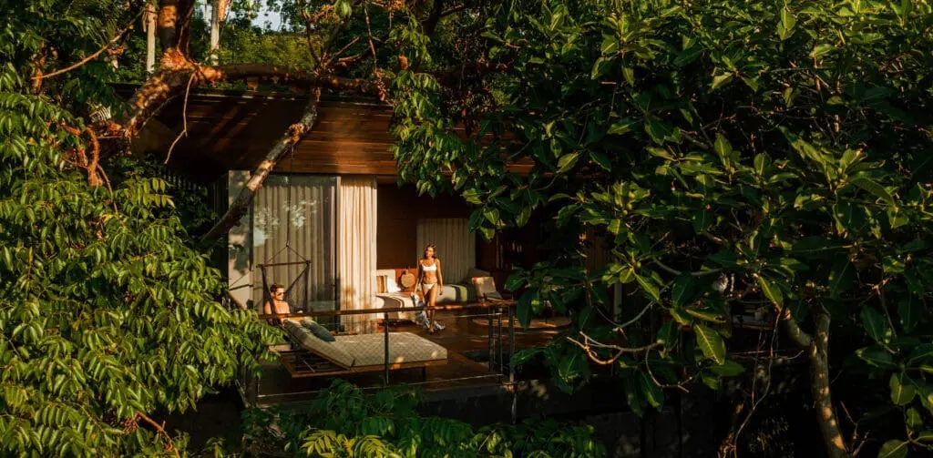 Couple relaxing on a wooden cabin balcony surrounded by greenery.