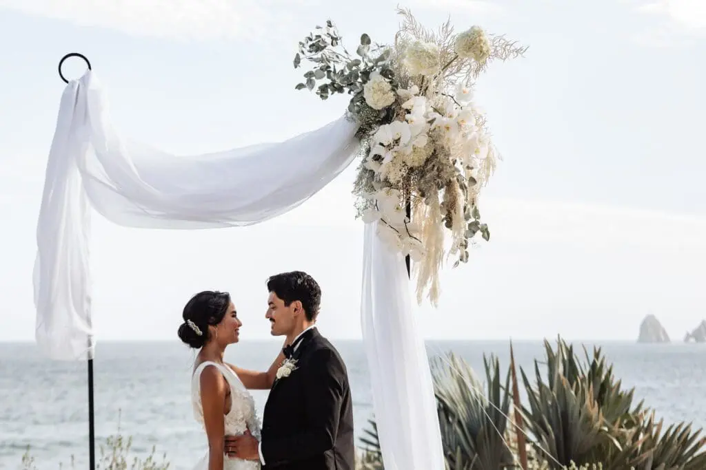 Bride and groom at a beach wedding ceremony under a floral arch