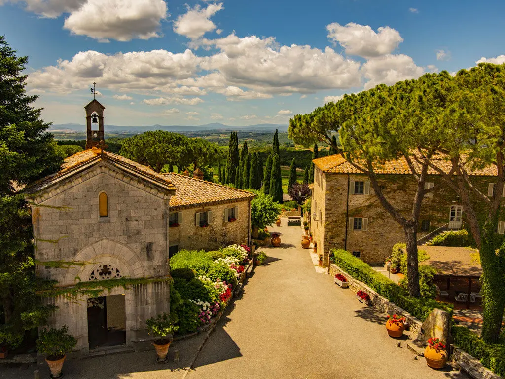 Tuscan borgo with stone buildings and a bell tower under a blue sky with clouds. Property descriptions meaning.