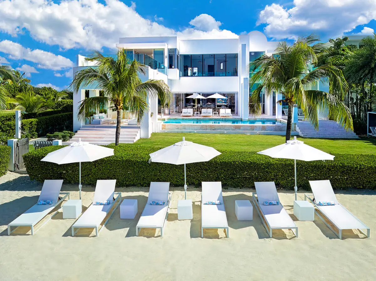 Luxury beachfront villa with pool, lounge chairs, and umbrellas. Property descriptions meaning.