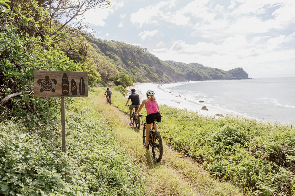 Cyclists on a trail at Rancho Santana, near the beach. Sign with turtle and surfboard icons.