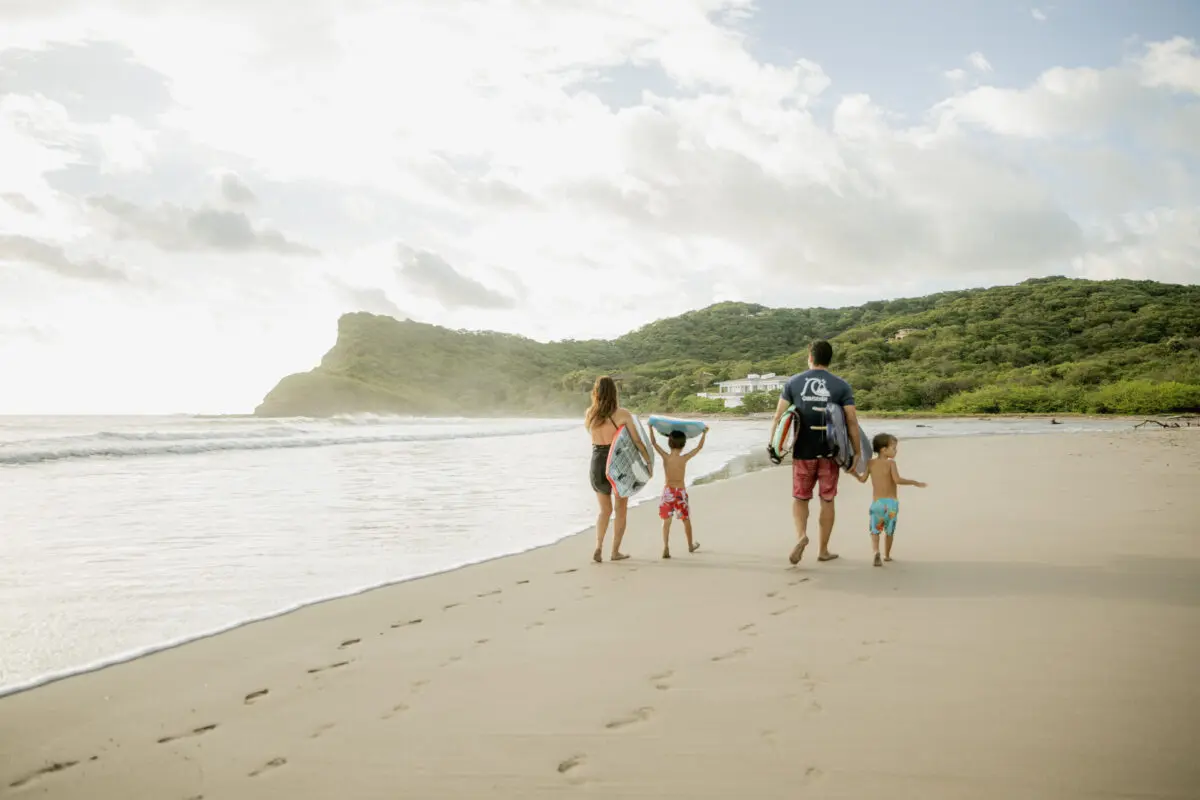 Family walking on a Rancho Santana beach with surfboards and boogie boards.
