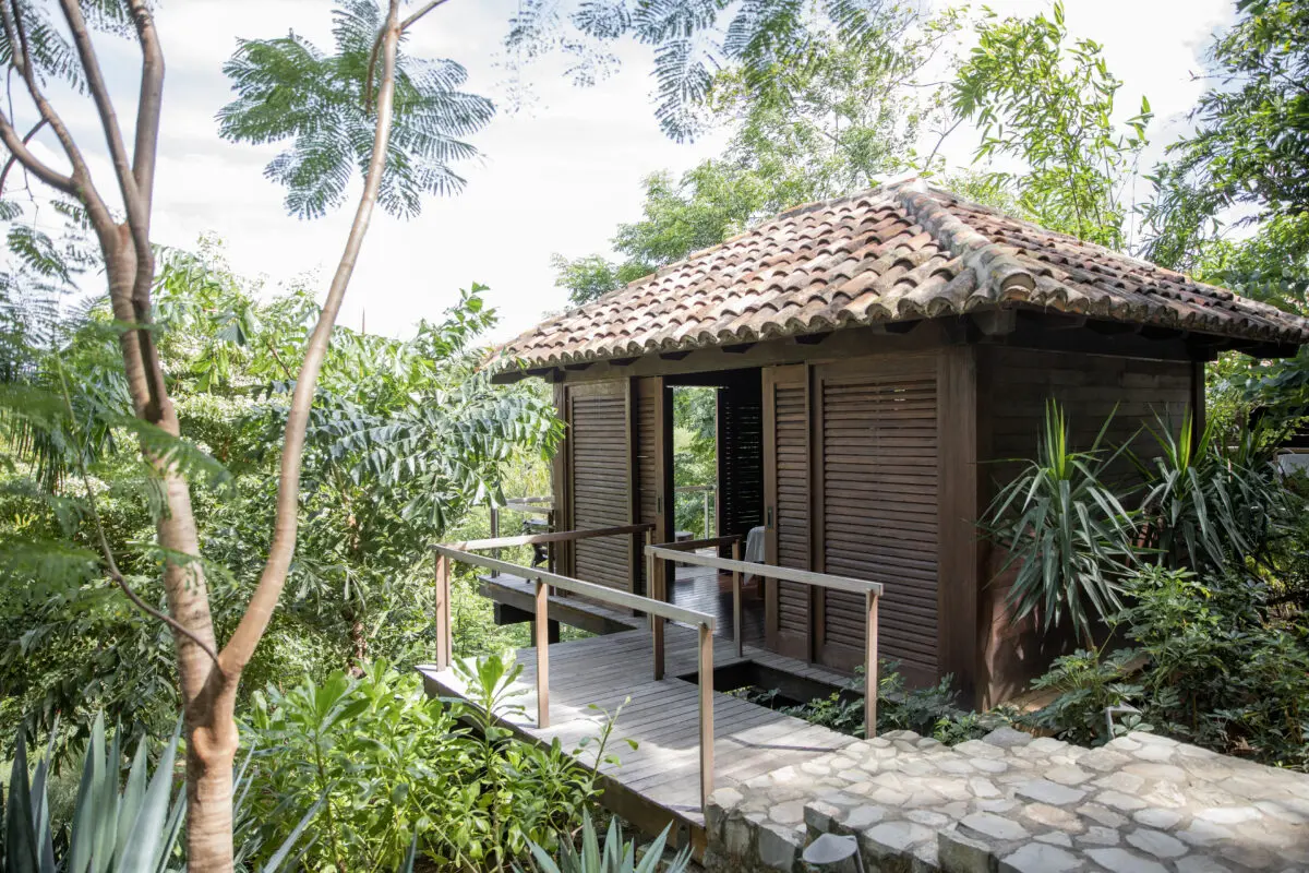 Wooden cabin with clay tile roof surrounded by lush greenery at Rancho Santana