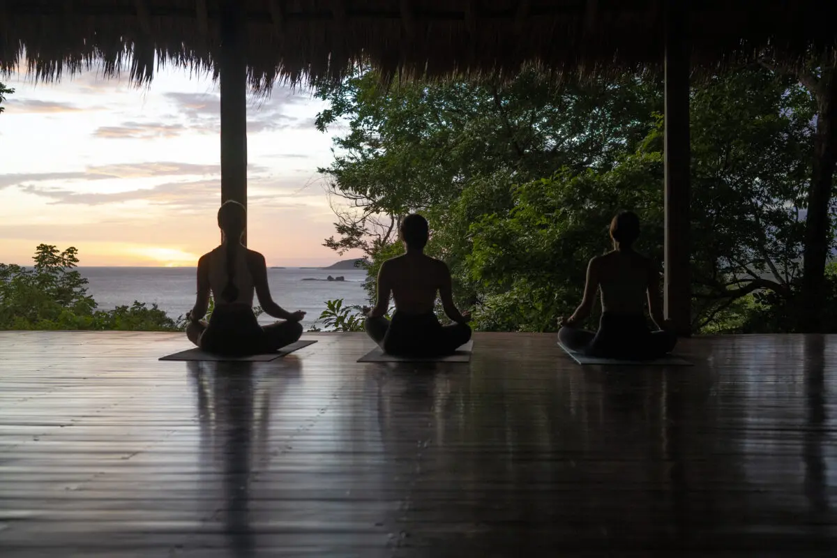 Rancho Santana: Silhouetted women meditating in a yoga studio overlooking the ocean at sunset.