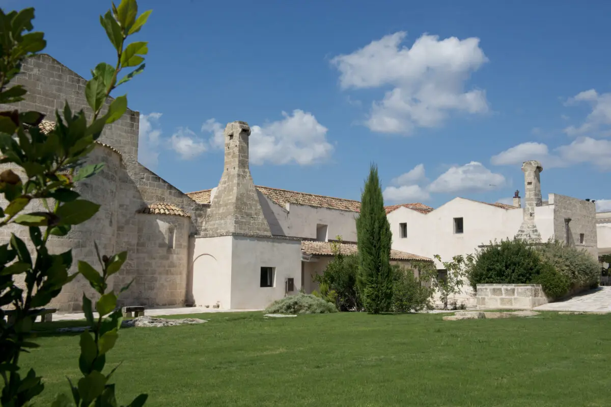 Relais Histò Hotel & SPA courtyard view with stone buildings, green lawn, and blue sky.