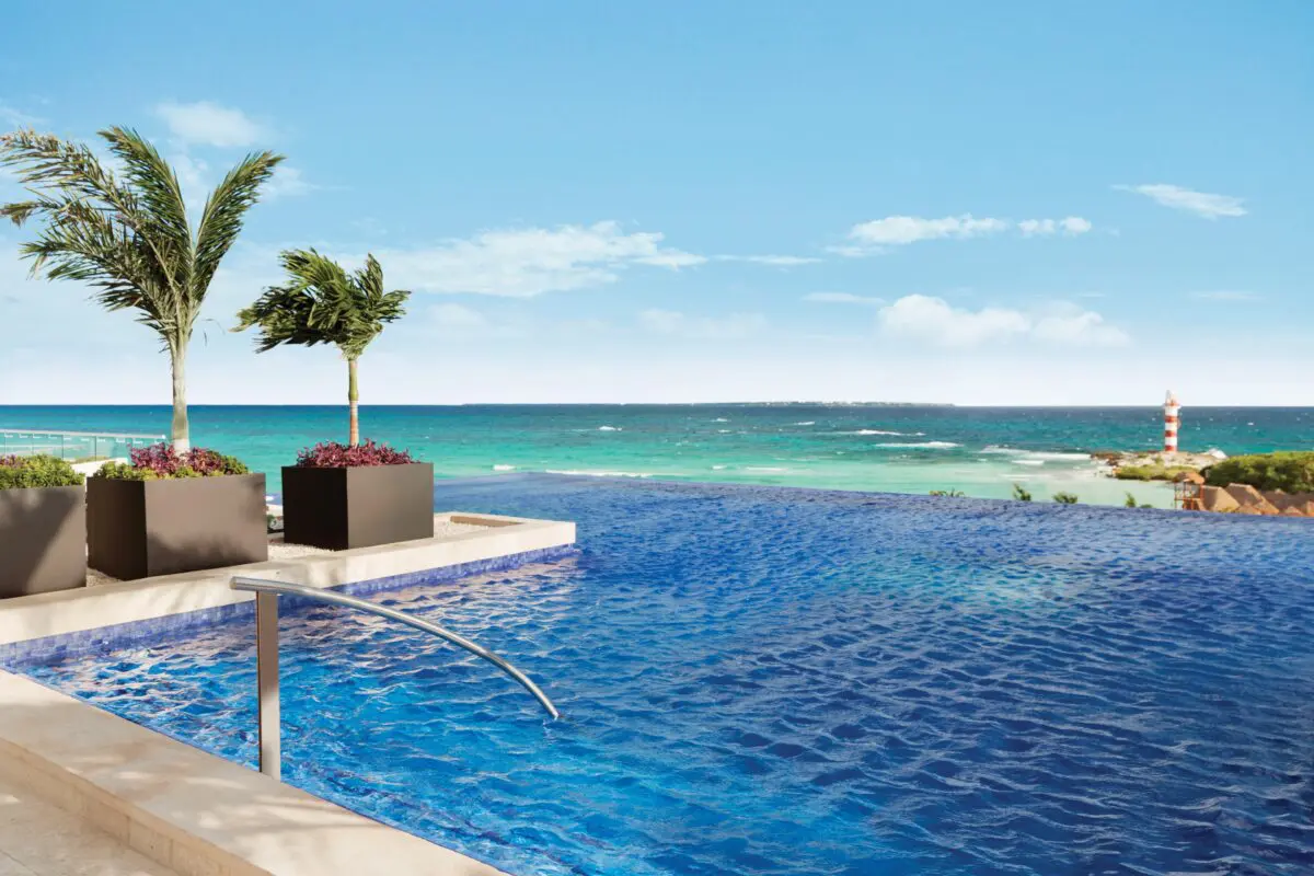 Infinity pool at Hyatt Ziva Cancun, a luxury wedding venue, overlooking the turquoise ocean and a red and white lighthouse.