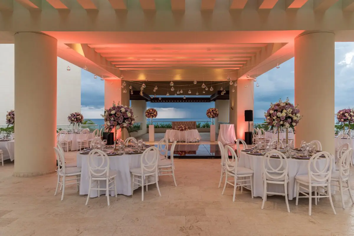 Luxury wedding venue in Cancun: Elegant reception setup with white tables, chairs, and floral centerpieces overlooking the ocean.