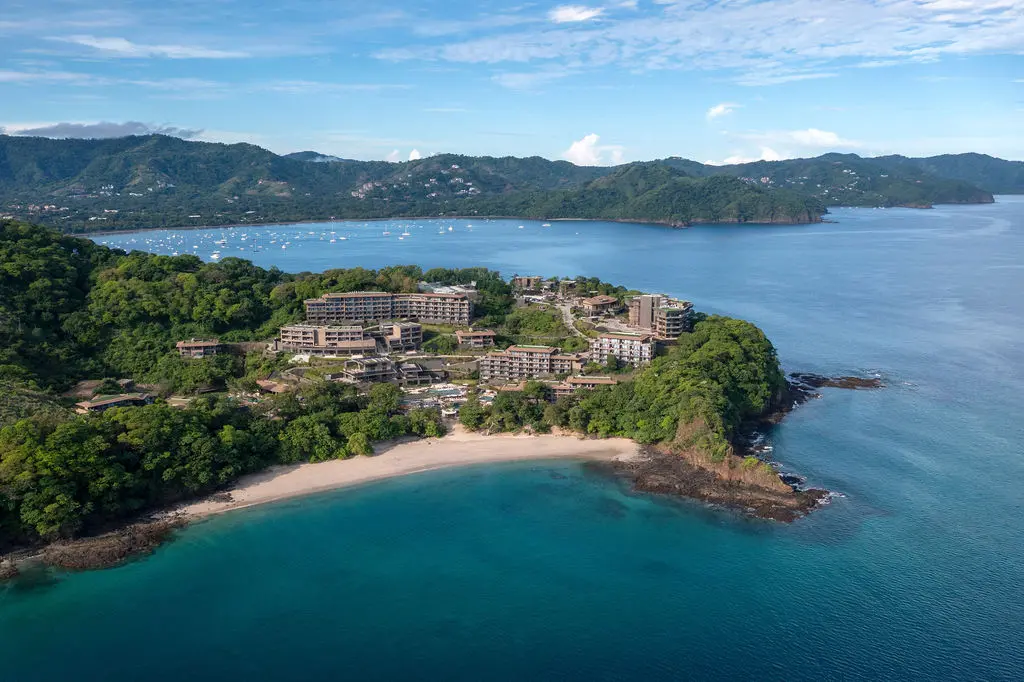 Aerial view of the Waldorf Astoria Costa Rica resort on a lush peninsula with a sandy beach and turquoise water.