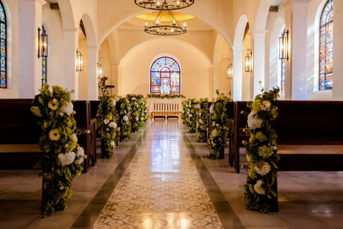 Church aisle decorated with flowers for a wedding at Rancho Santana, featuring stained glass and pews.