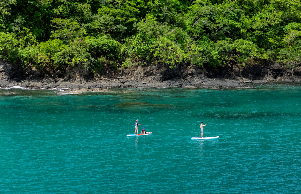Paddleboarding in turquoise waters near lush coastline, Waldorf Astoria Costa Rica.
