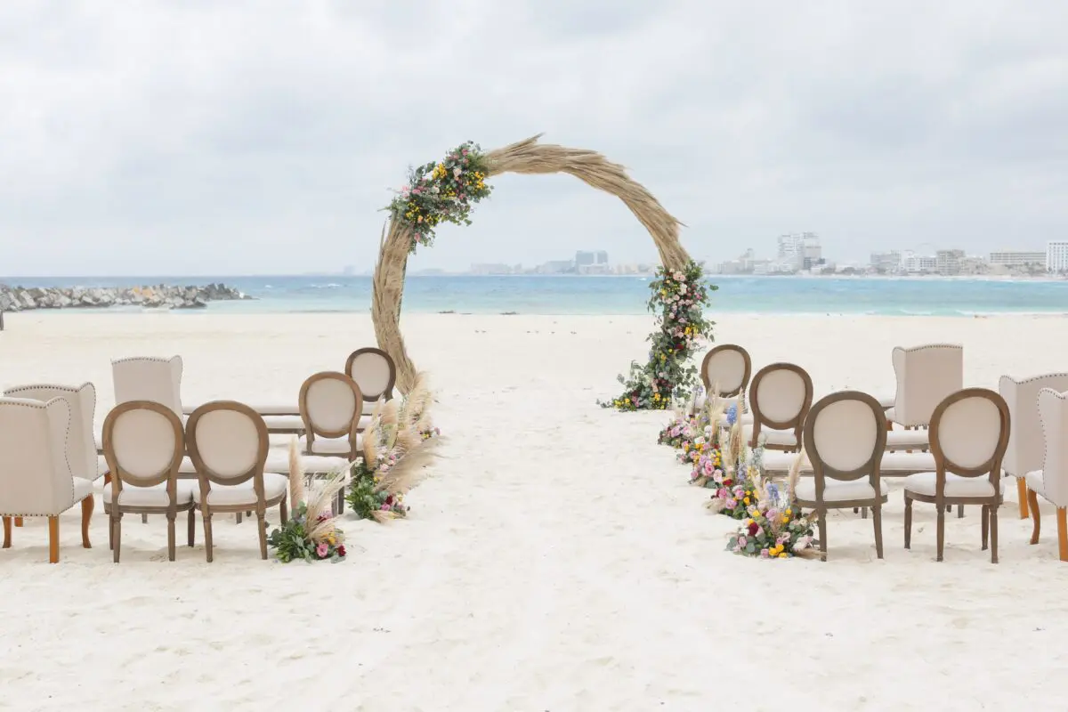 Beach wedding setup at Hyatt Ziva Cancun. Circular arch with flowers, chairs on white sand. Luxury wedding venue.
