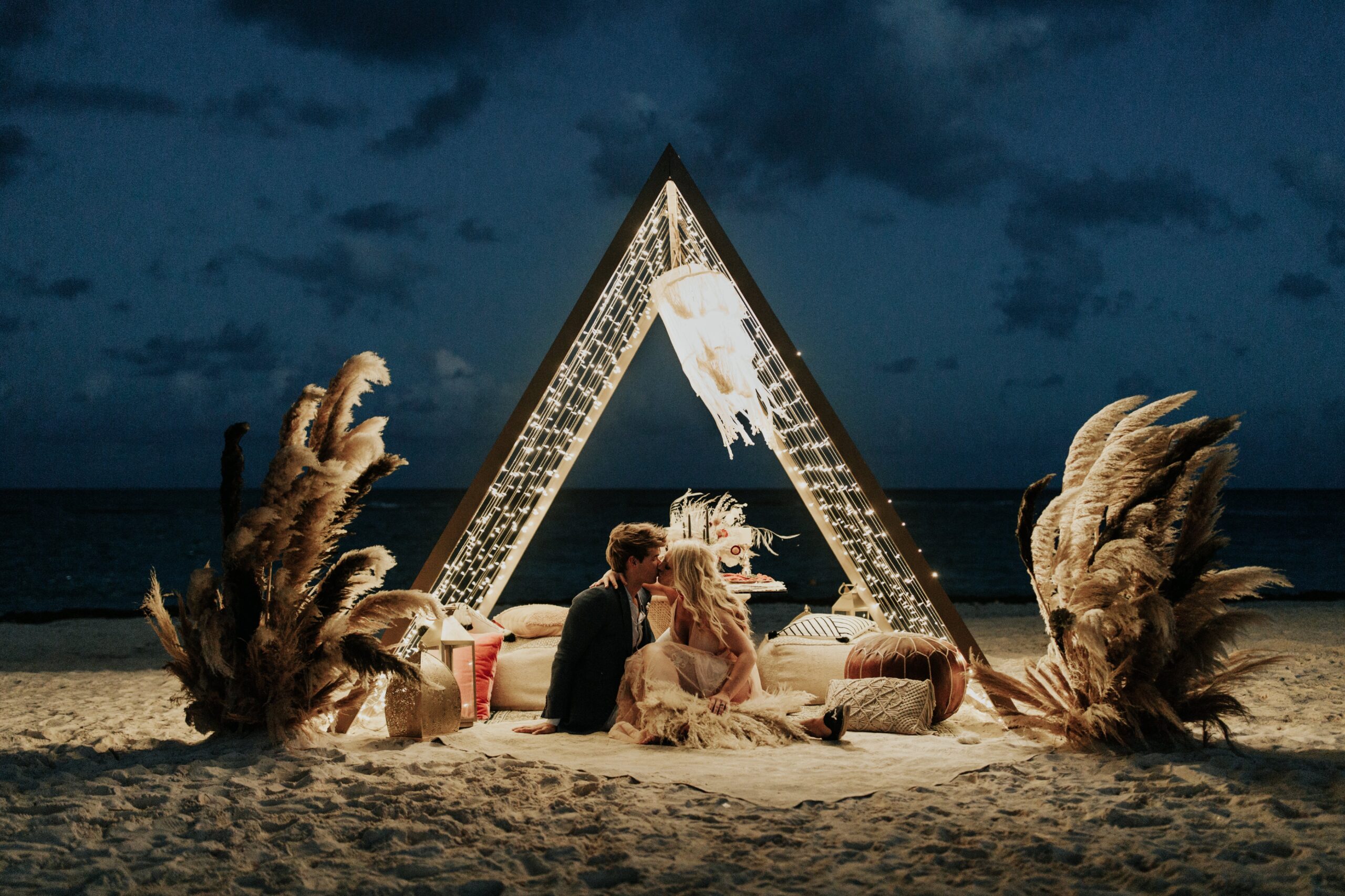 Couple kissing under a lit triangle on a beach at night, Riviera Maya Ceremonies