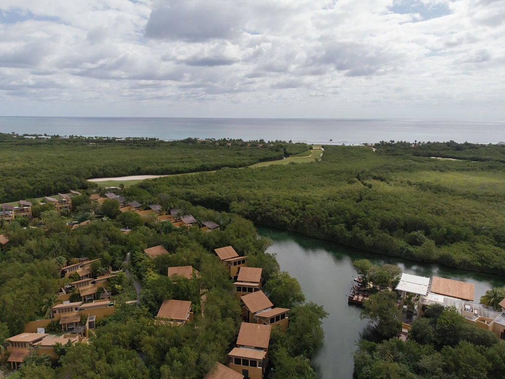 Aerial view of Banyan Tree Mayakoba resort along a river, with the Riviera Maya coastline in the distance.