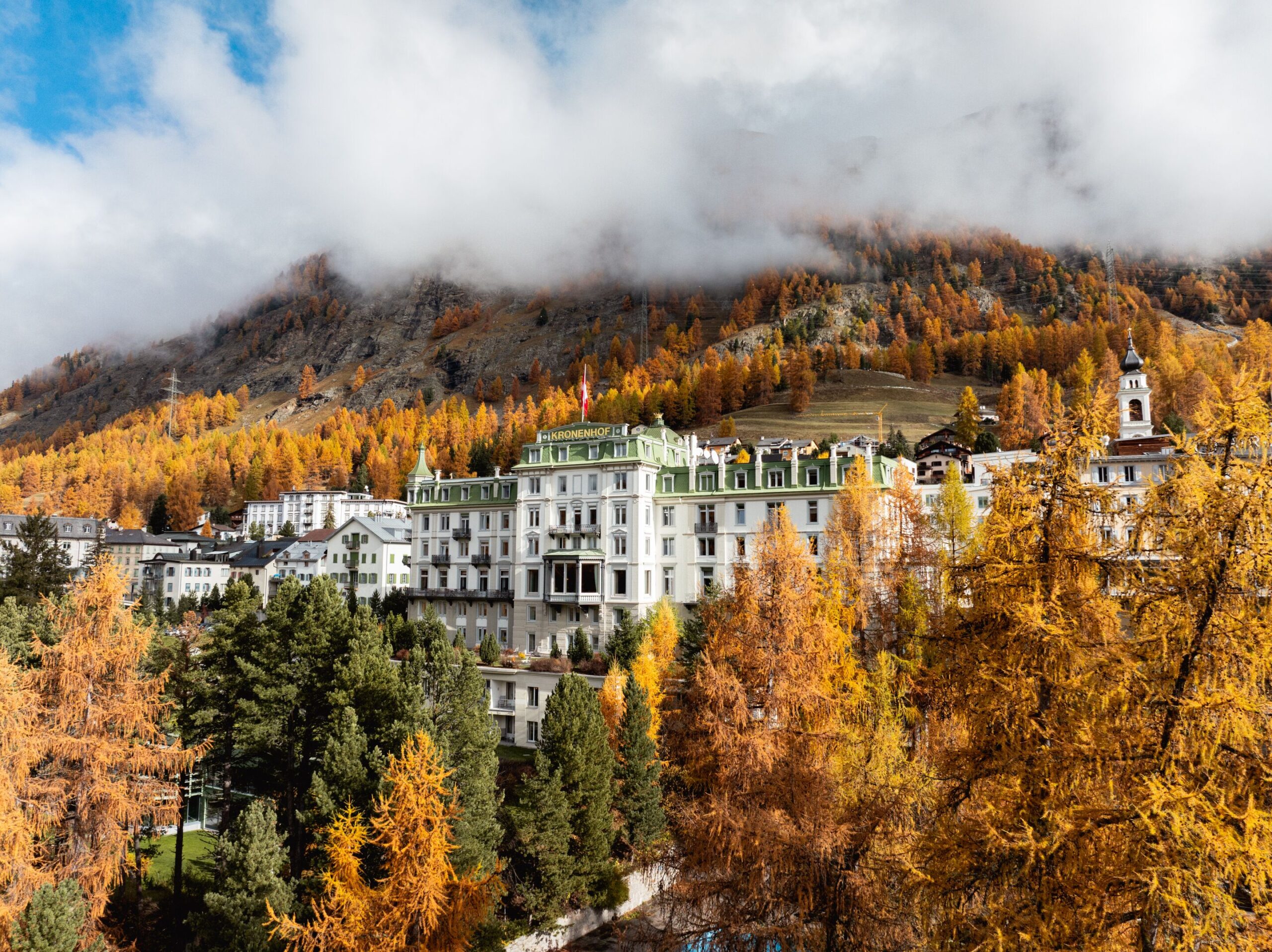 Grand Hotel Kronenhof in the Swiss Alps during autumn, surrounded by golden trees and mountains.