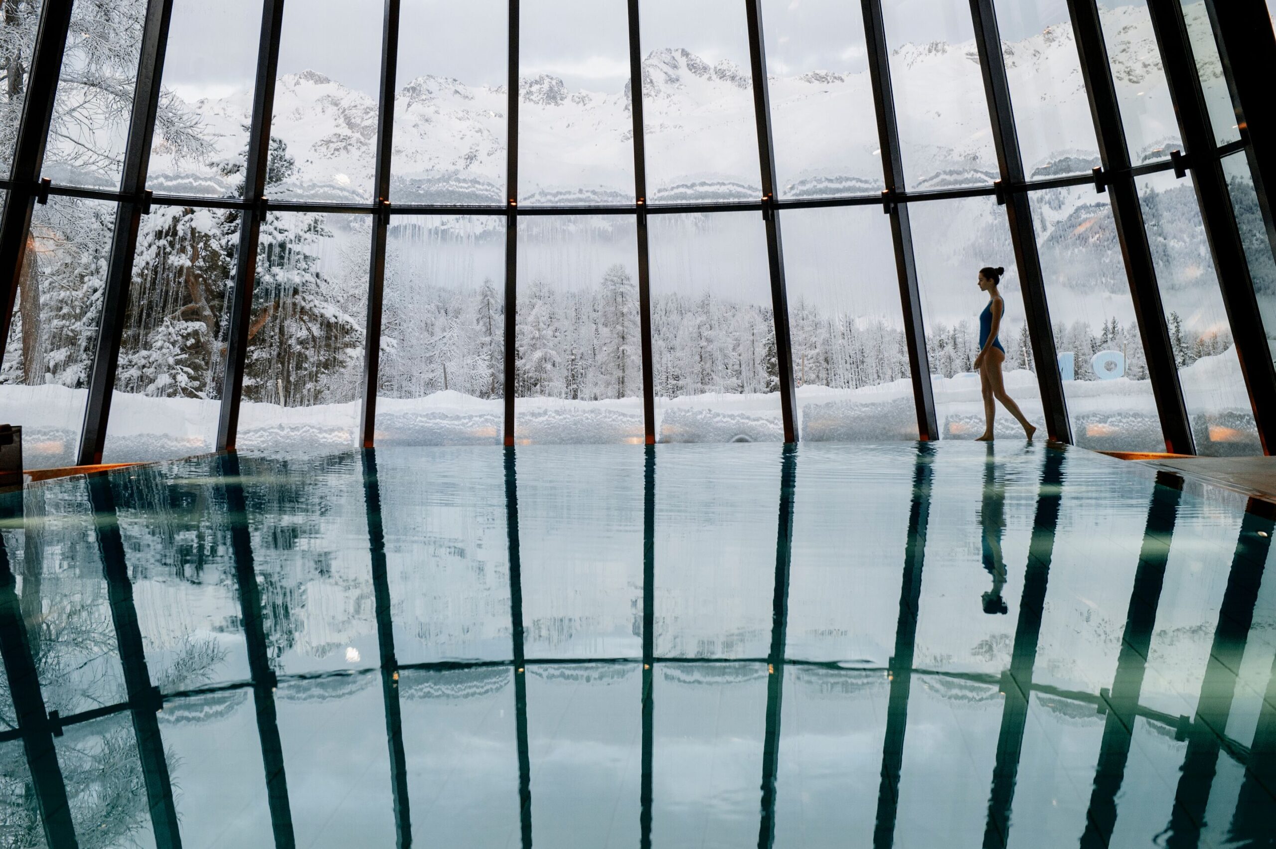 Woman at Grand Hotel Kronenhof indoor pool with Swiss Alps view. Winter scene.