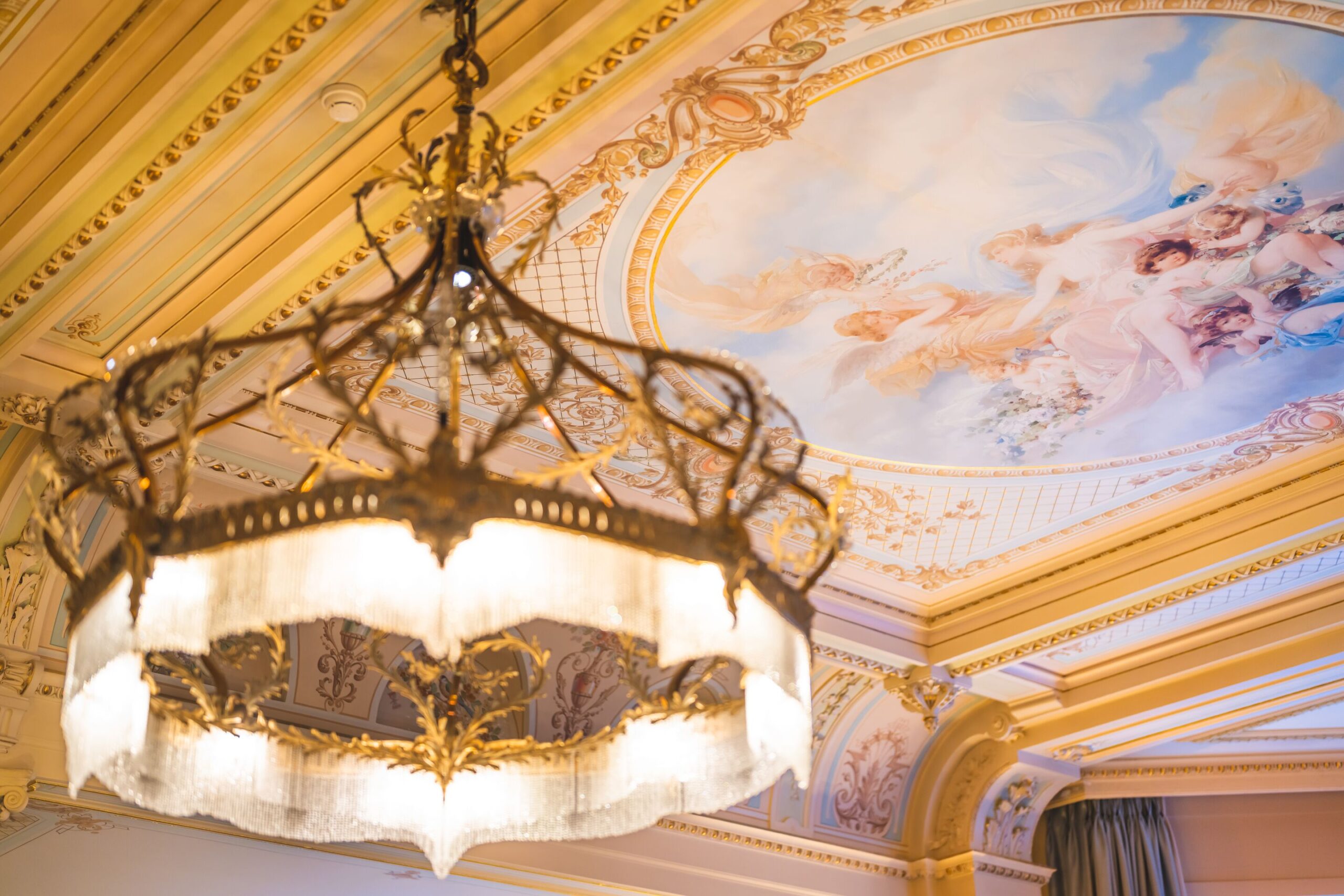 Ornate chandelier hangs beneath a ceiling fresco in the Grand Hotel Kronenhof, a venue for a Swiss Alps wedding.