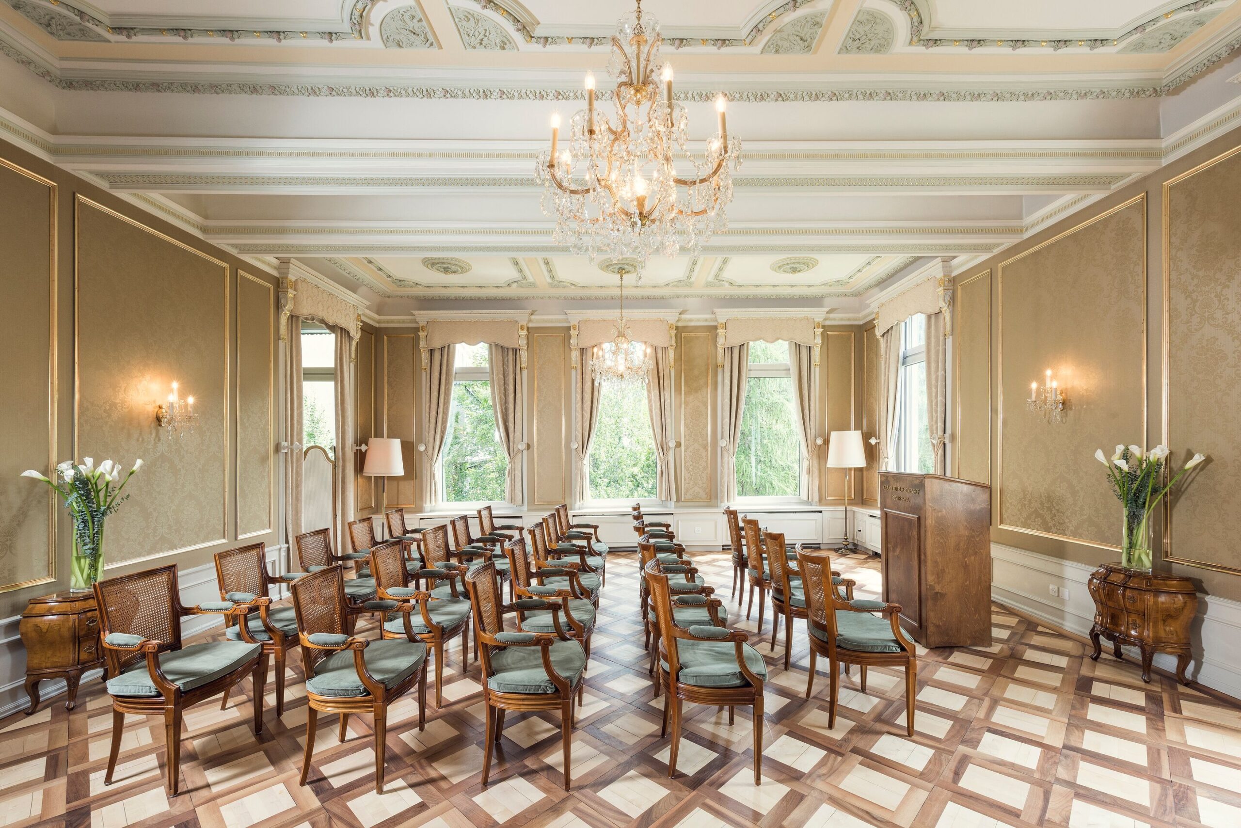 Elegant room setup for a Swiss Alps wedding at Grand Hotel Kronenhof, featuring a chandelier, podium, and seating.
