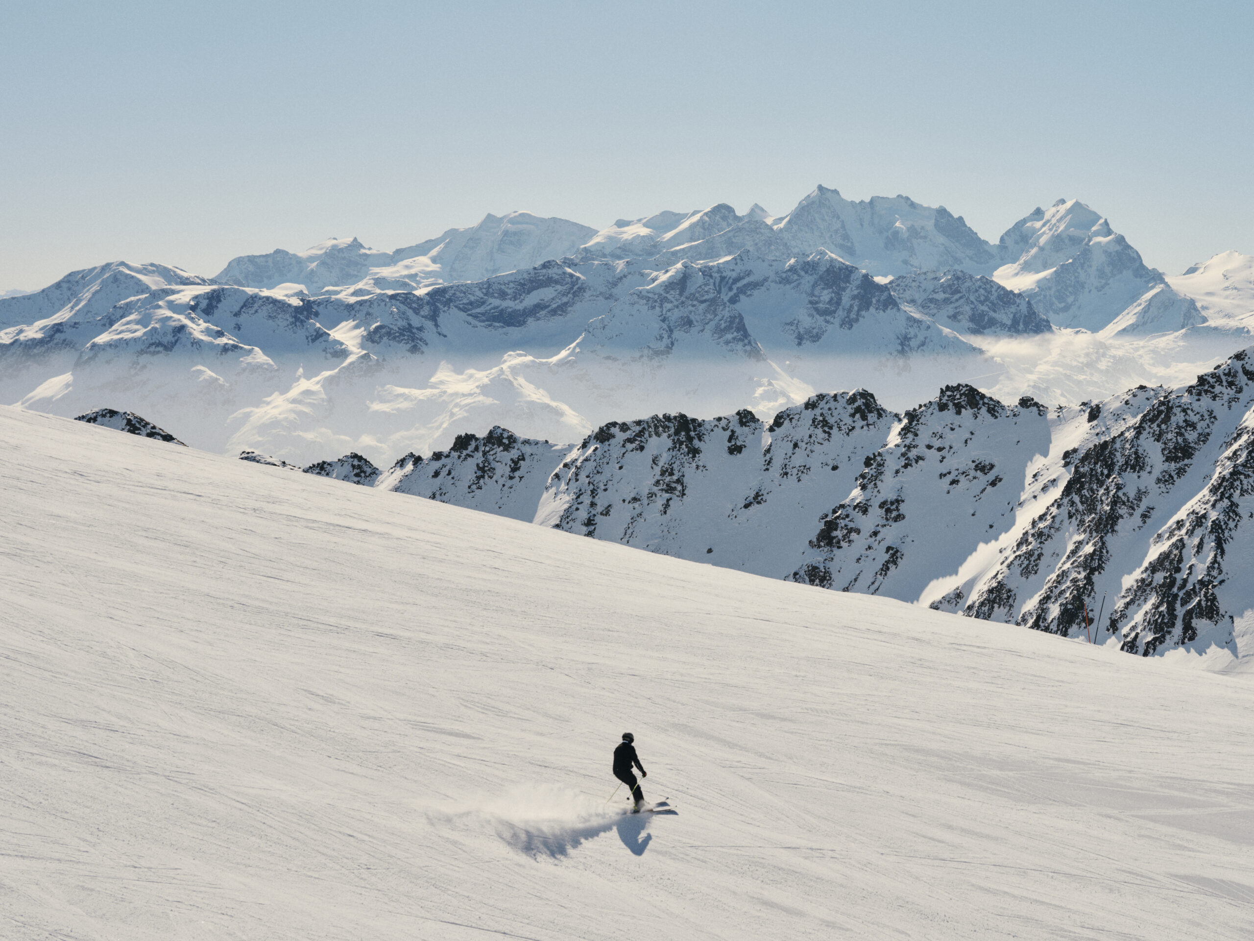 Skier on a groomed slope in the Swiss Alps, with majestic mountains in the background.