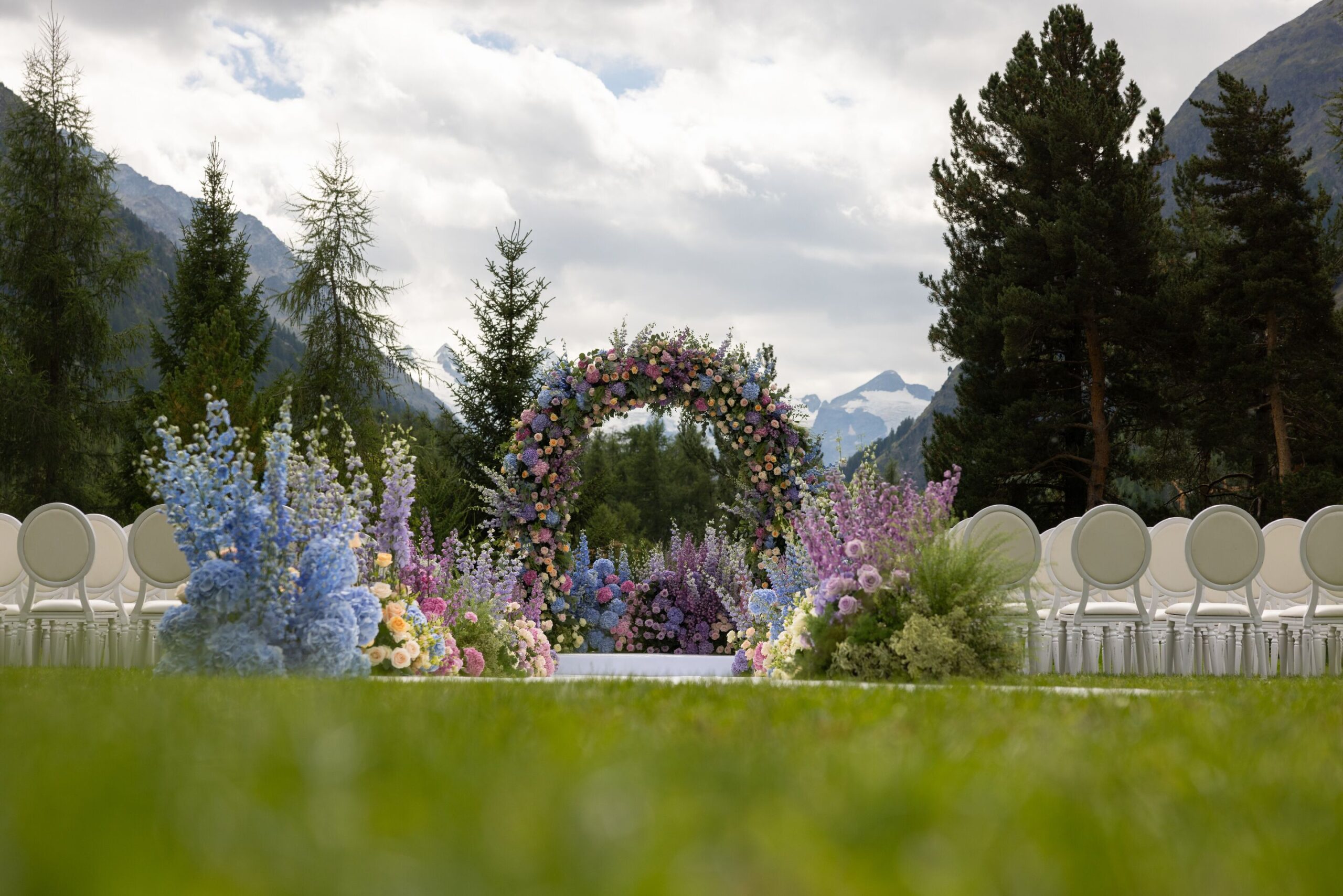 Swiss Alps wedding ceremony with floral archway and white chairs at the Grand Hotel Kronenhof.