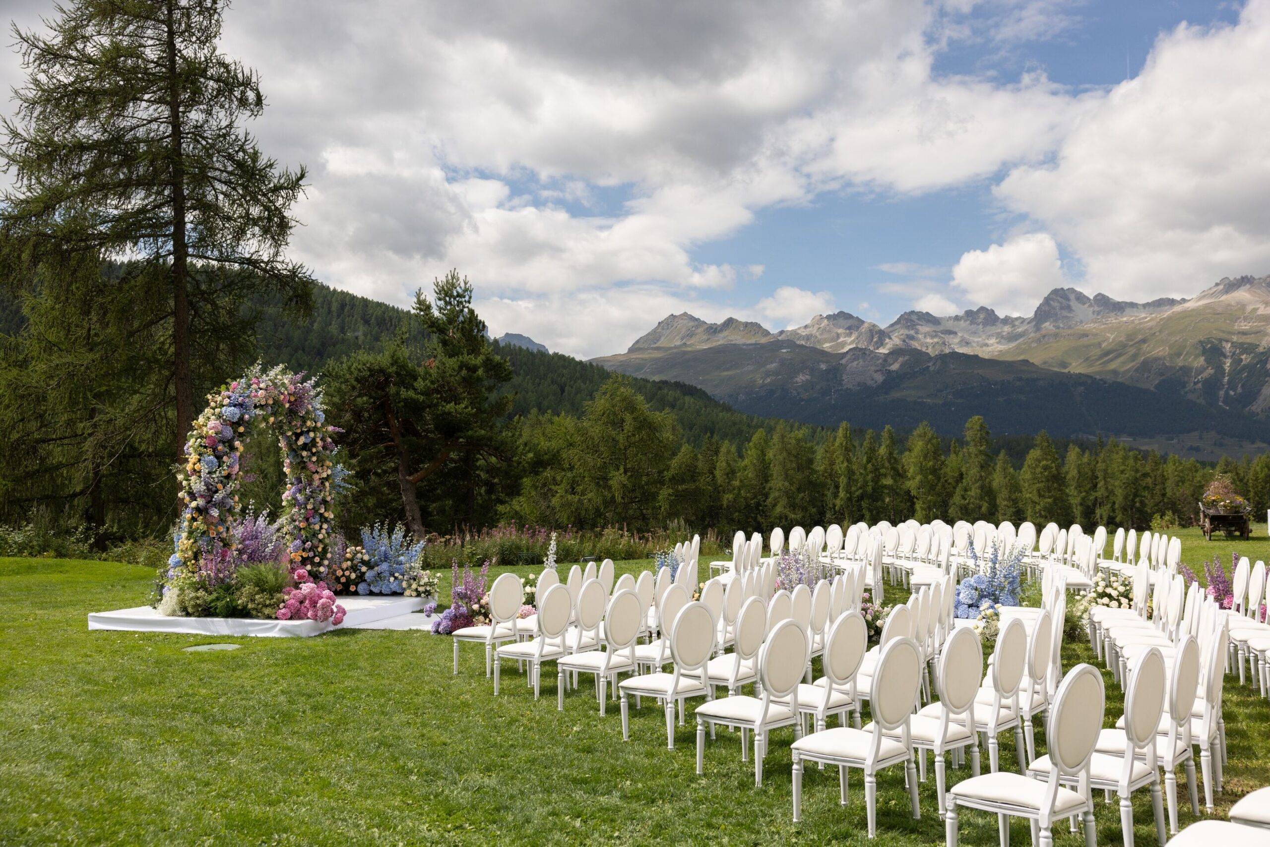 Swiss Alps wedding at Grand Hotel Kronenhof. Outdoor ceremony with white chairs and floral arch.