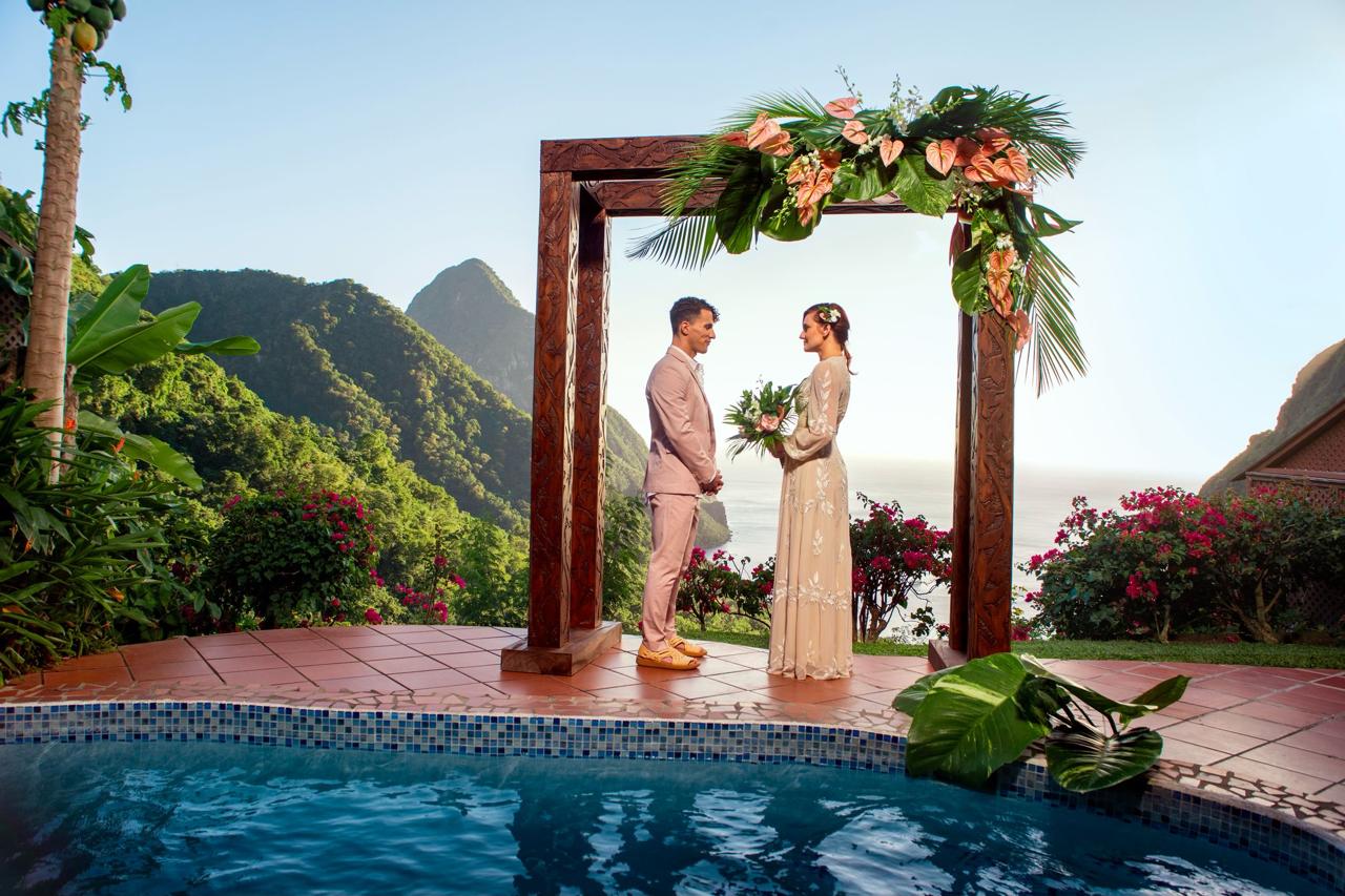 Island wedding at Ladera Resort, St. Lucia. Bride and groom under floral arch with Pitons view.