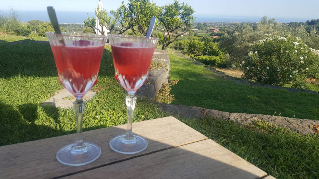 2 prepared cocktails on a ledge with the Sicilian countryside in the background