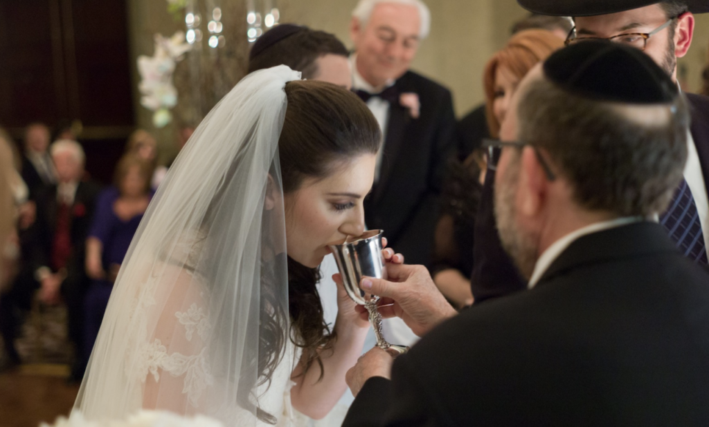 Jewish bride drinking from kiddush cup under chuppah