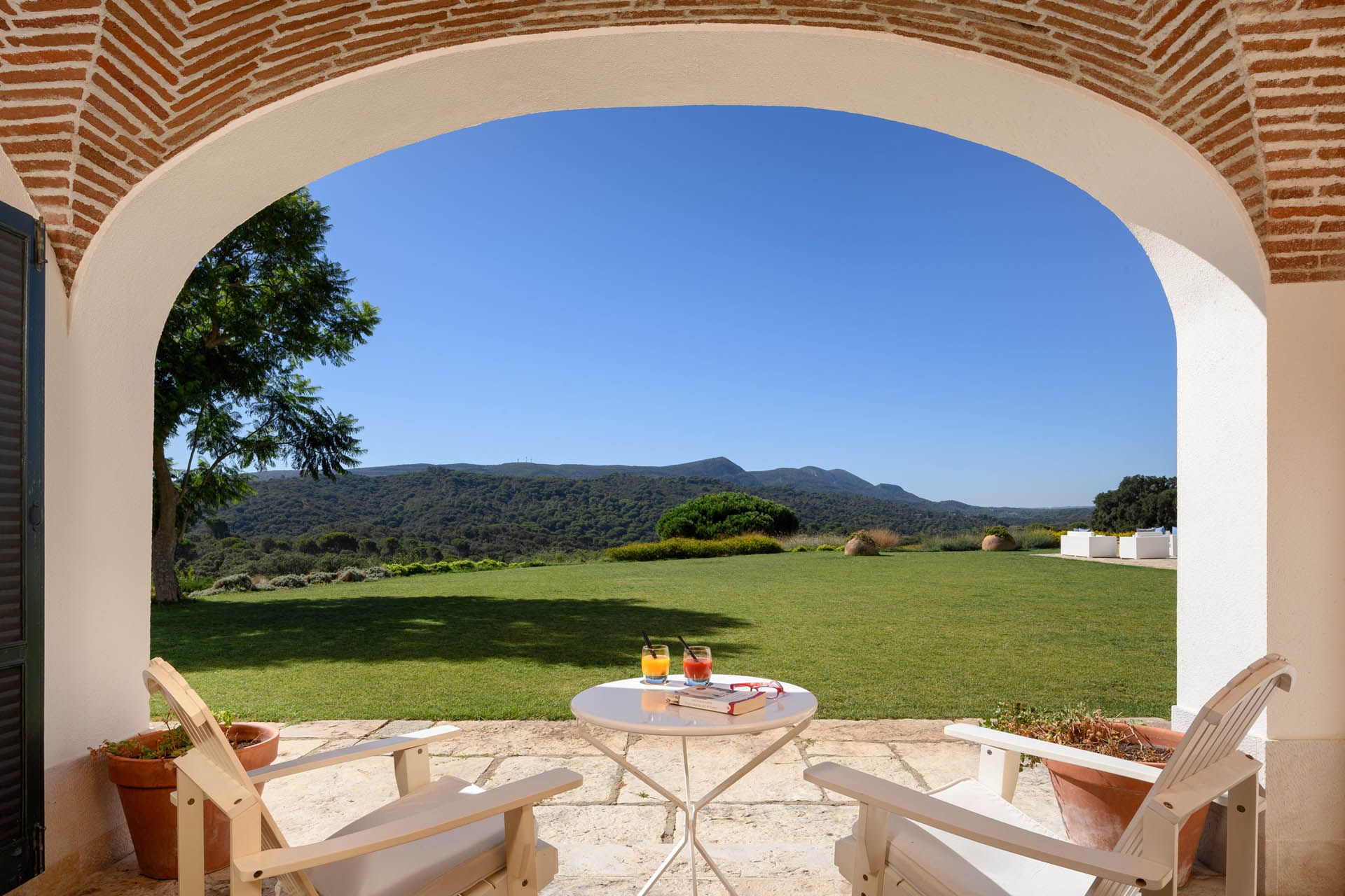 Arched open space with 2 chairs overlooking a green landscape and hillside.