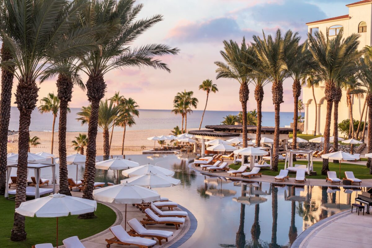 Luxury resort pool at Hilton Los Cabos with palm trees, lounge chairs, and ocean view, perfect for a Los Cabos destination wedding.