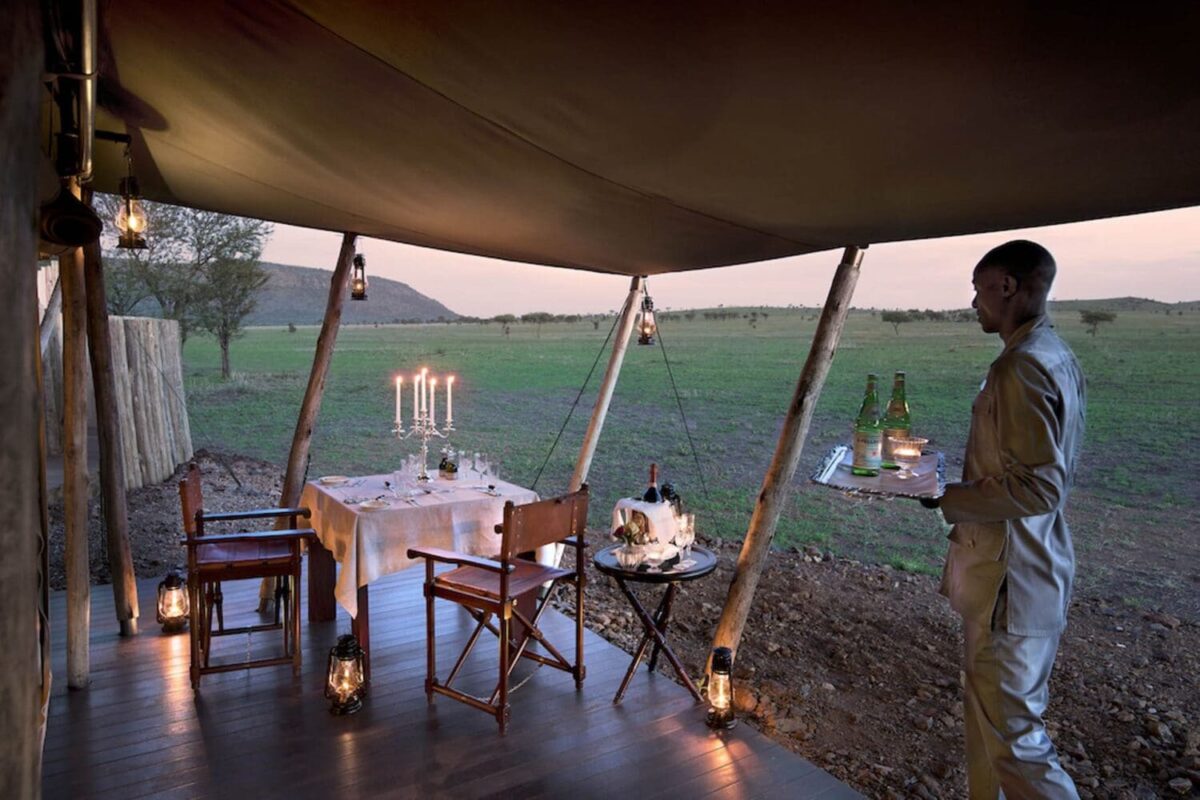 Luxury safari honeymoon dining setup with candles and a server in African savannah