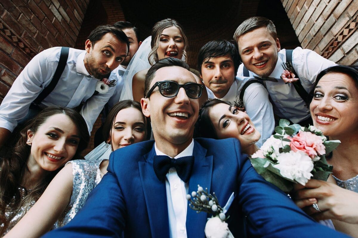 Group of friends taking a selfie at a wedding, smiling and holding flowers