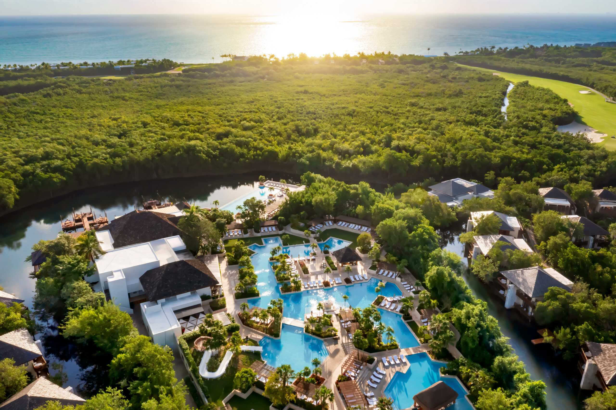 Fairmont Mayakoba resort aerial view with pools, lush greenery, and ocean at sunrise. Ideal for a Riviera Maya Beach Wedding.