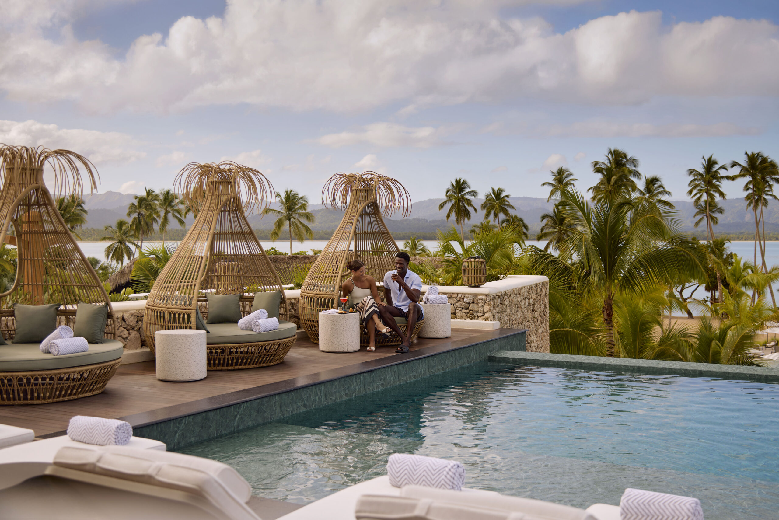 Couple at Zemi Miches All-Inclusive Resort pool, relaxing in lounge chairs.