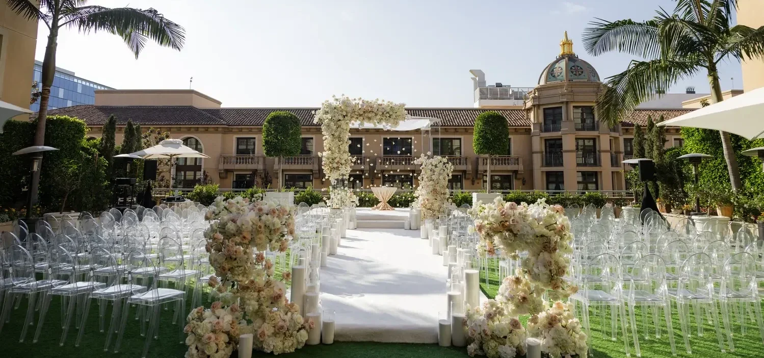 Elegant outdoor wedding ceremony setup at the Maybourne Beverly Hills, featuring a floral arch and clear ghost chairs.