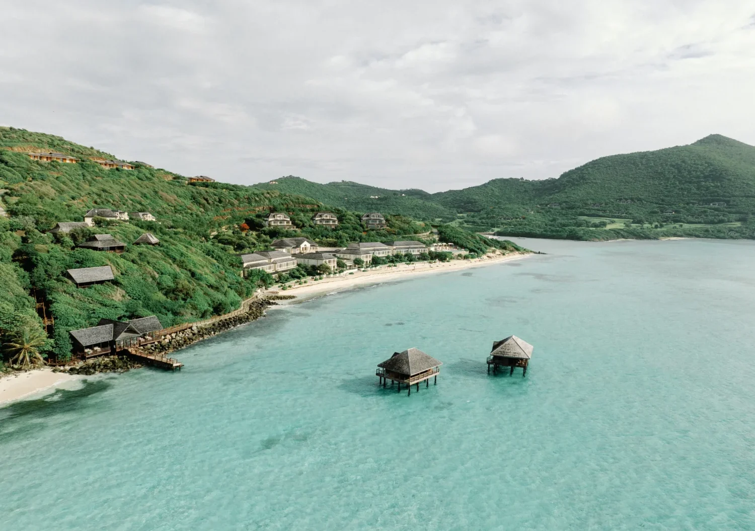 Aerial view of luxury resort on a tropical beach with overwater bungalows.