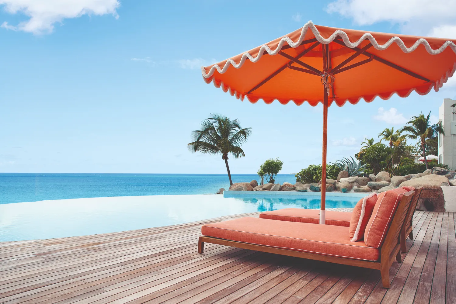 Luxury lounge chairs and orange umbrella at a Caribbean pool overlooking the ocean. Perfect for a destination wedding at La Samanna, a Belmond Hotel.
