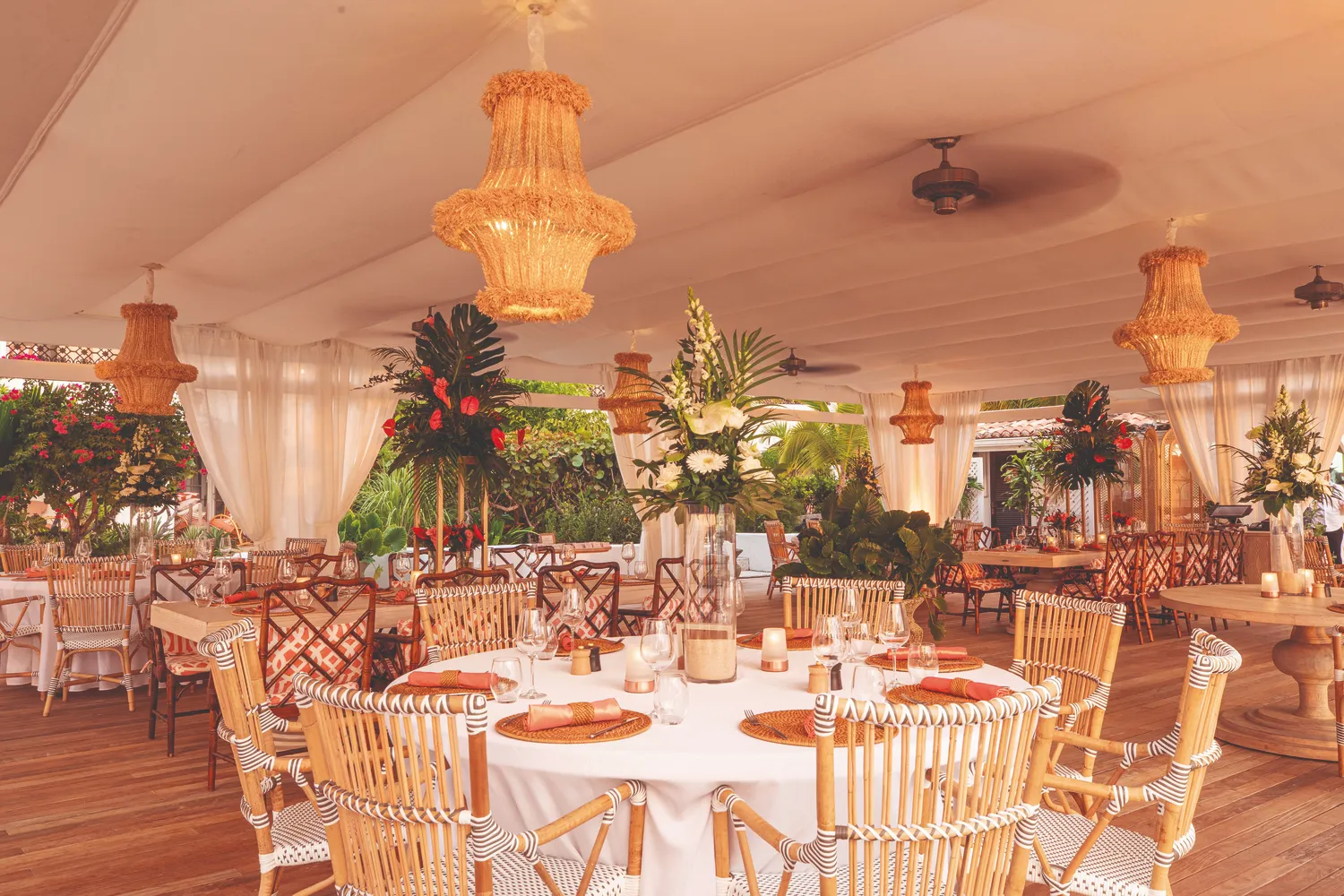 Elegant Caribbean destination wedding reception at La Samanna, a Belmond Hotel. Tables with rattan chairs and tropical floral arrangements.