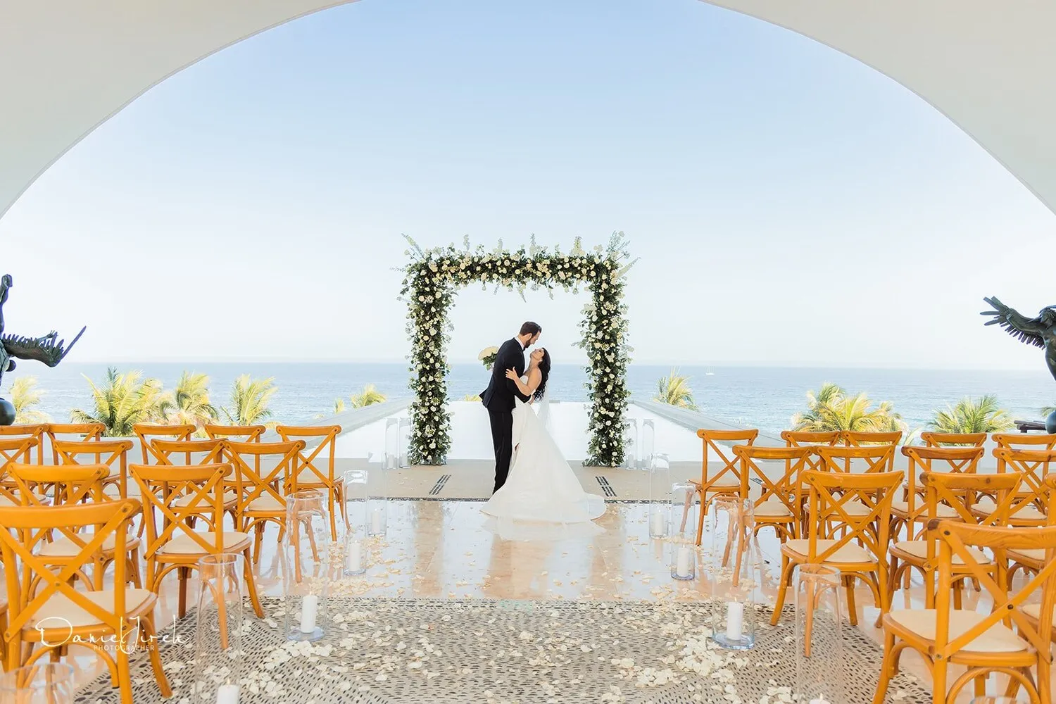 Bride and groom embrace at their Los Cabos wedding ceremony, beneath a floral arch overlooking the ocean.