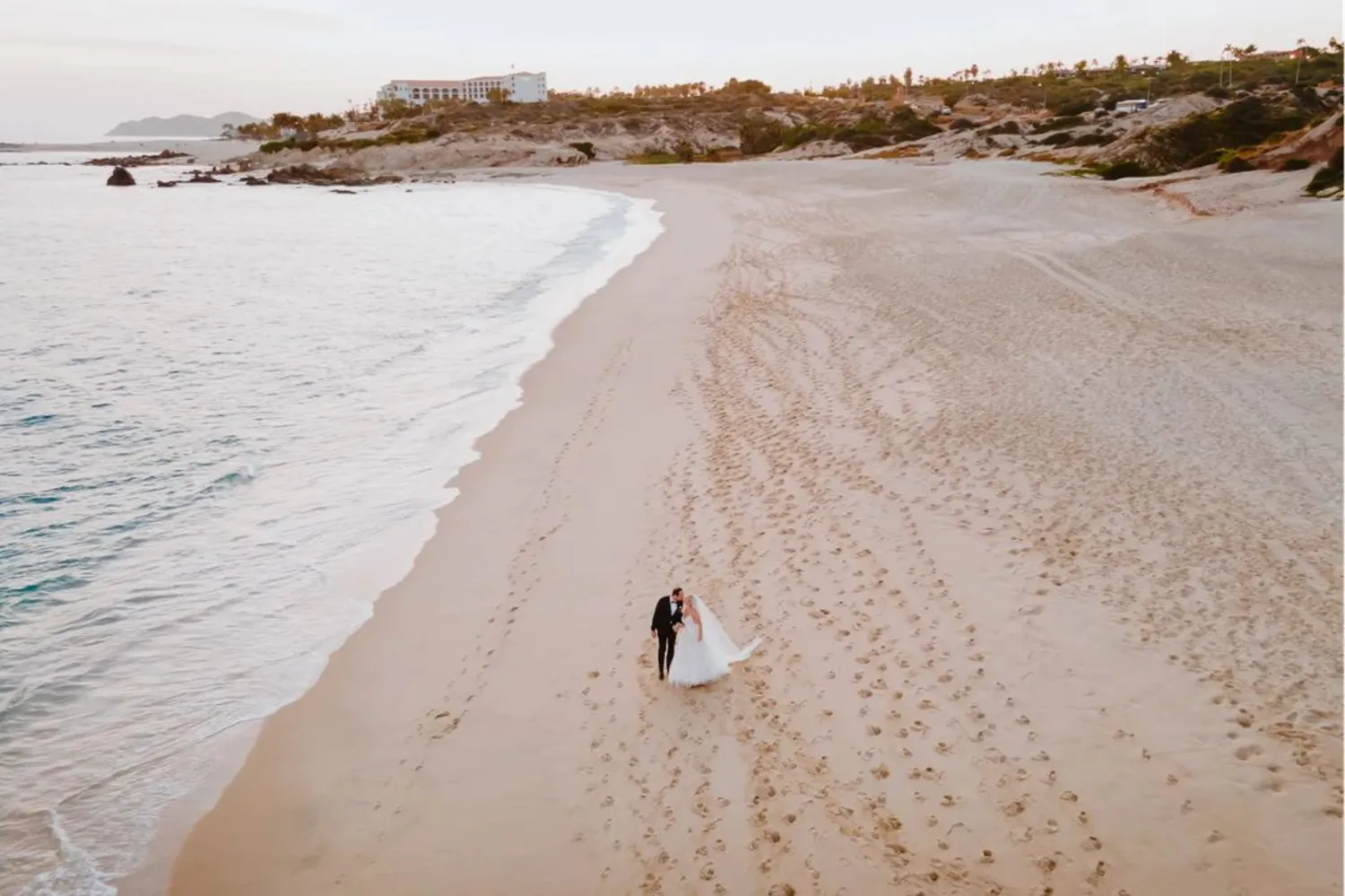 Bride and groom walking on a Los Cabos beach toward the ocean. Marquis Los Cabos wedding destination.