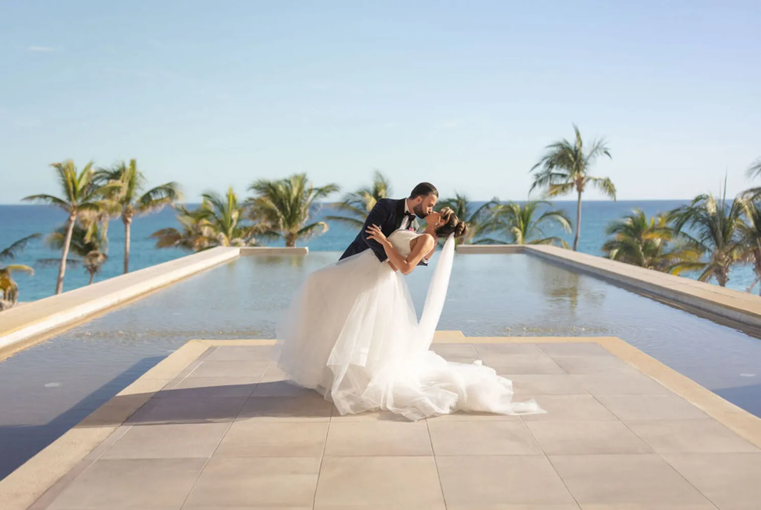 Bride and groom kissing by a pool at a Los Cabos wedding.