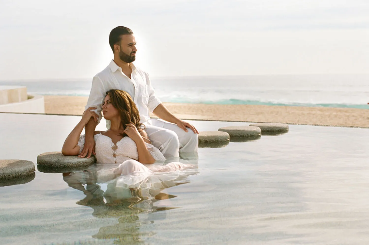 Couple in white attire relaxing by a pool at a Los Cabos wedding destination.