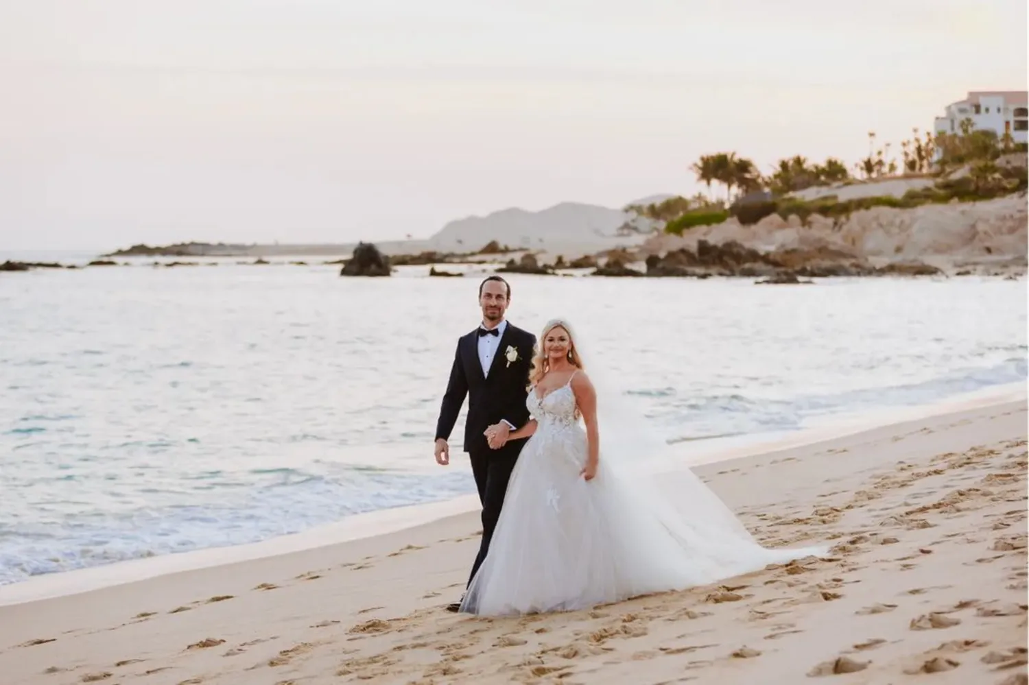 Happy couple holding hands on a Los Cabos beach during their wedding.