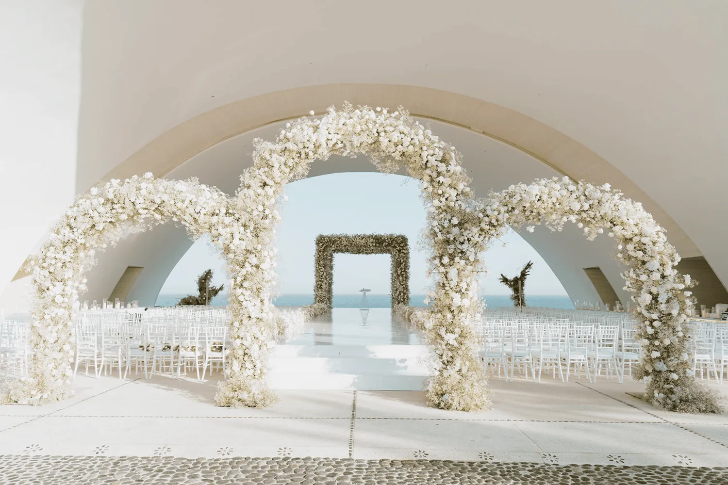 Elegant wedding ceremony setup at Marquis Los Cabos, featuring white floral arches and a stunning ocean view. Los Cabos wedding destination.