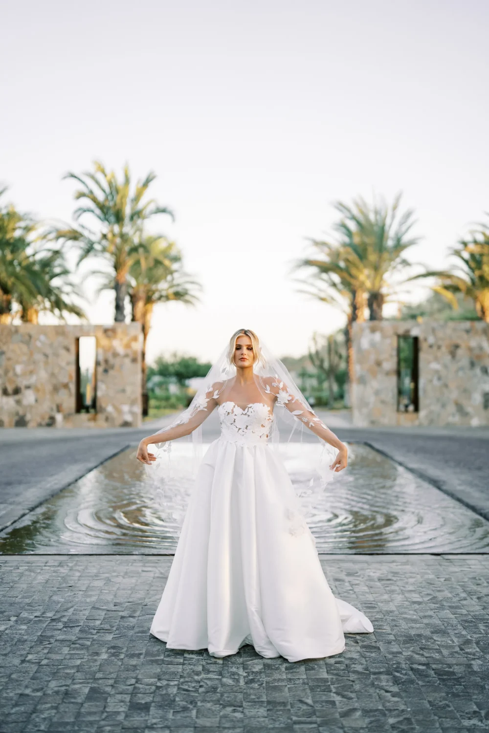 Bride in a white wedding gown poses for a styled shoot near a reflecting pool.